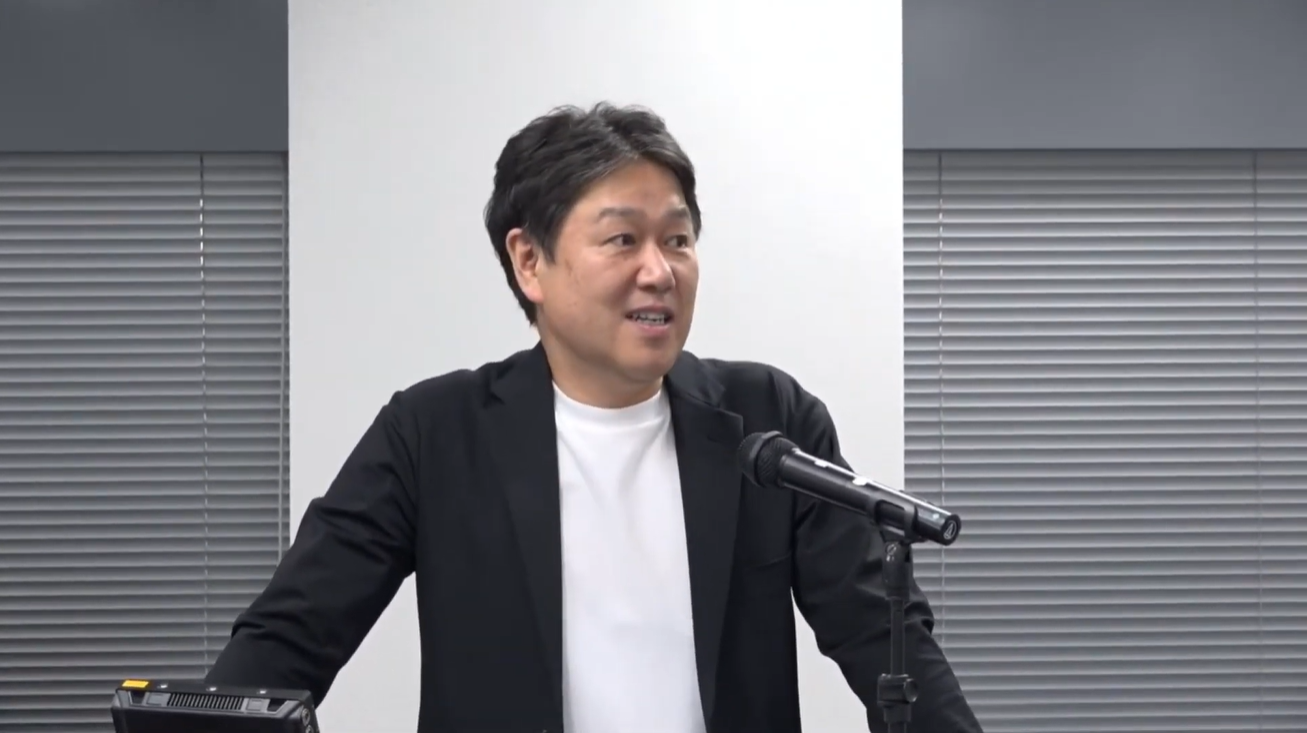 アズームの菅田代表取締役社長が登壇し、話している様子